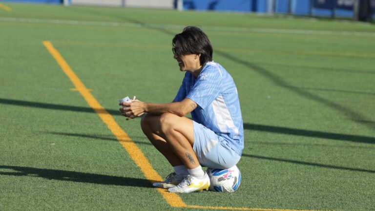 Sara Monforte sentada encima de un balón mirando a sus jugadoras entrenar